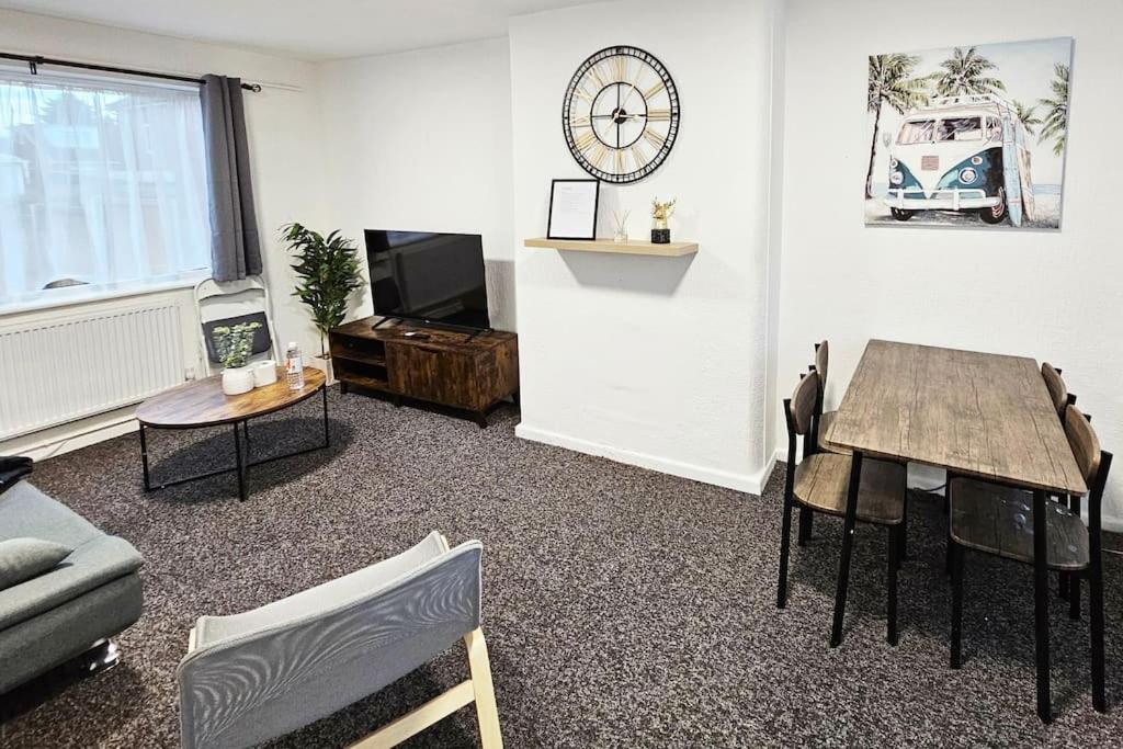 a living room with a table and a clock on the wall at Swinton, Manchester (2) in Manchester