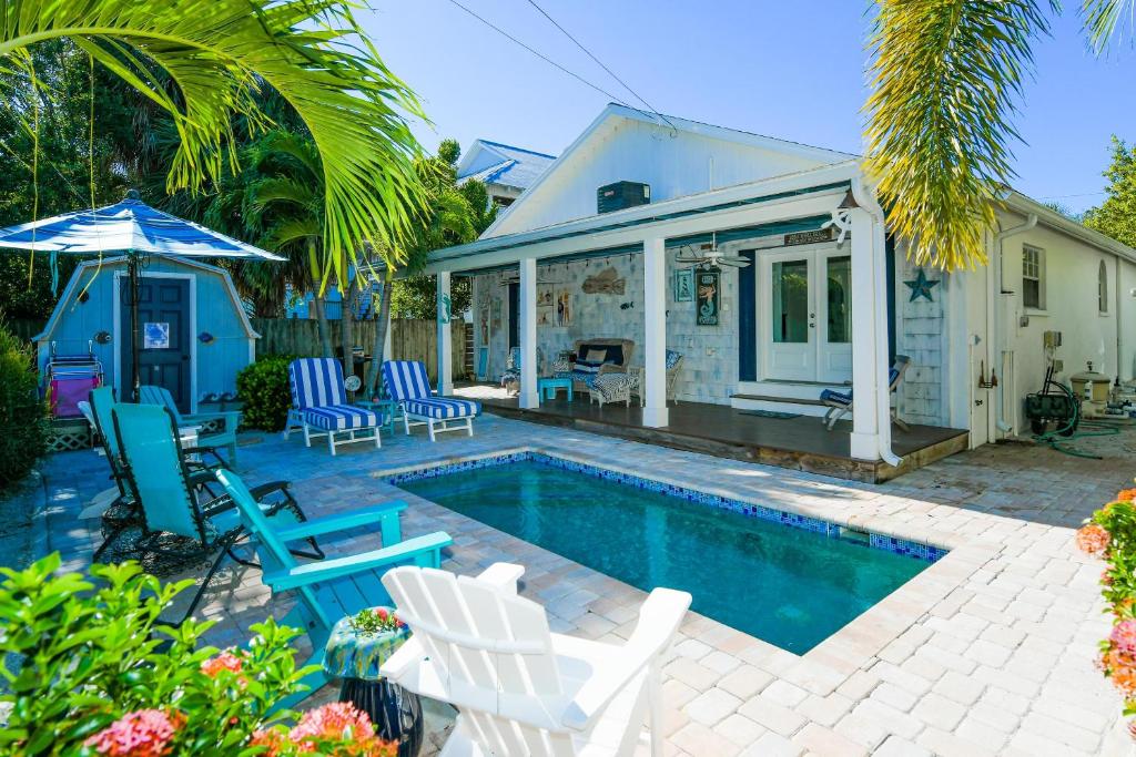 a swimming pool with chairs and a house at Buttonwood Cottage in Anna Maria