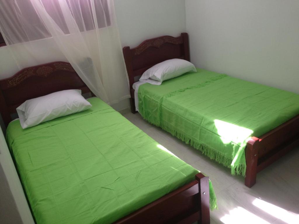 two beds in a room with green sheets at Hostal la Lomita in Popayan