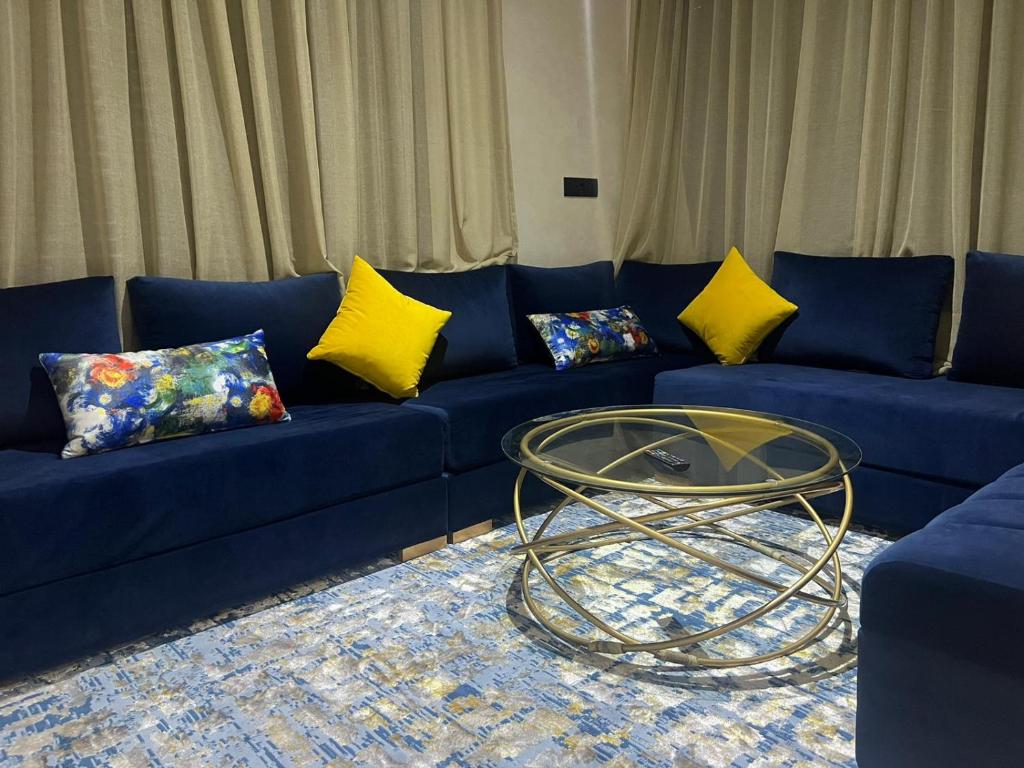 a blue couch with yellow pillows and a glass table at Résidence BAYTI in El Jadida