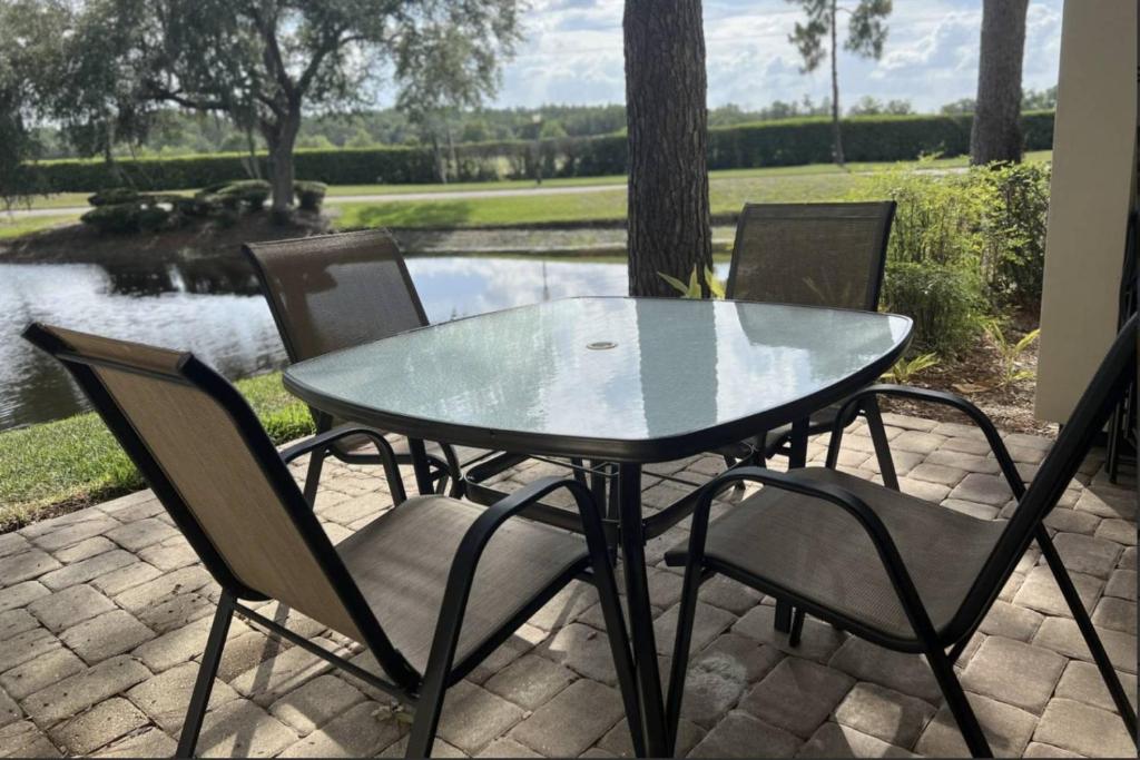 ein Glastisch und Stühle auf einer Terrasse mit einem Teich in der Unterkunft Peaceful Pond Paradise III ~ Ground Floor ~ Water Views in Wesley Chapel