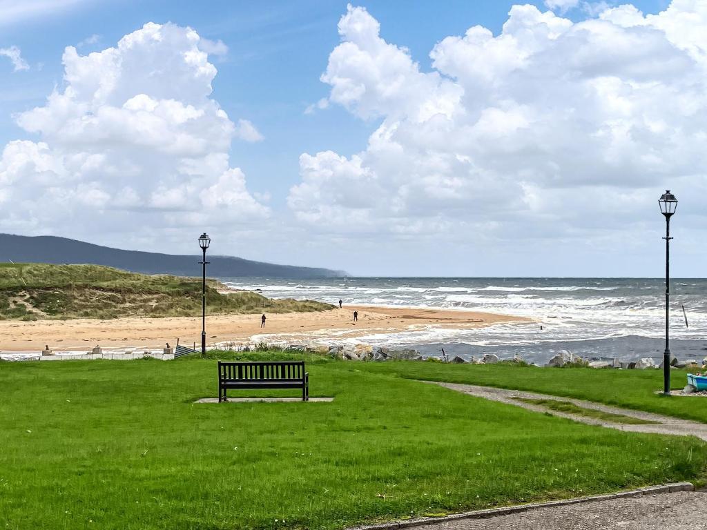 um banco de parque sentado na relva perto da praia em Beach Croft em Brora