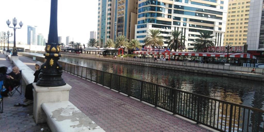 a river in a city with buildings and a pole at Masat El Sharjah for men in Sharjah