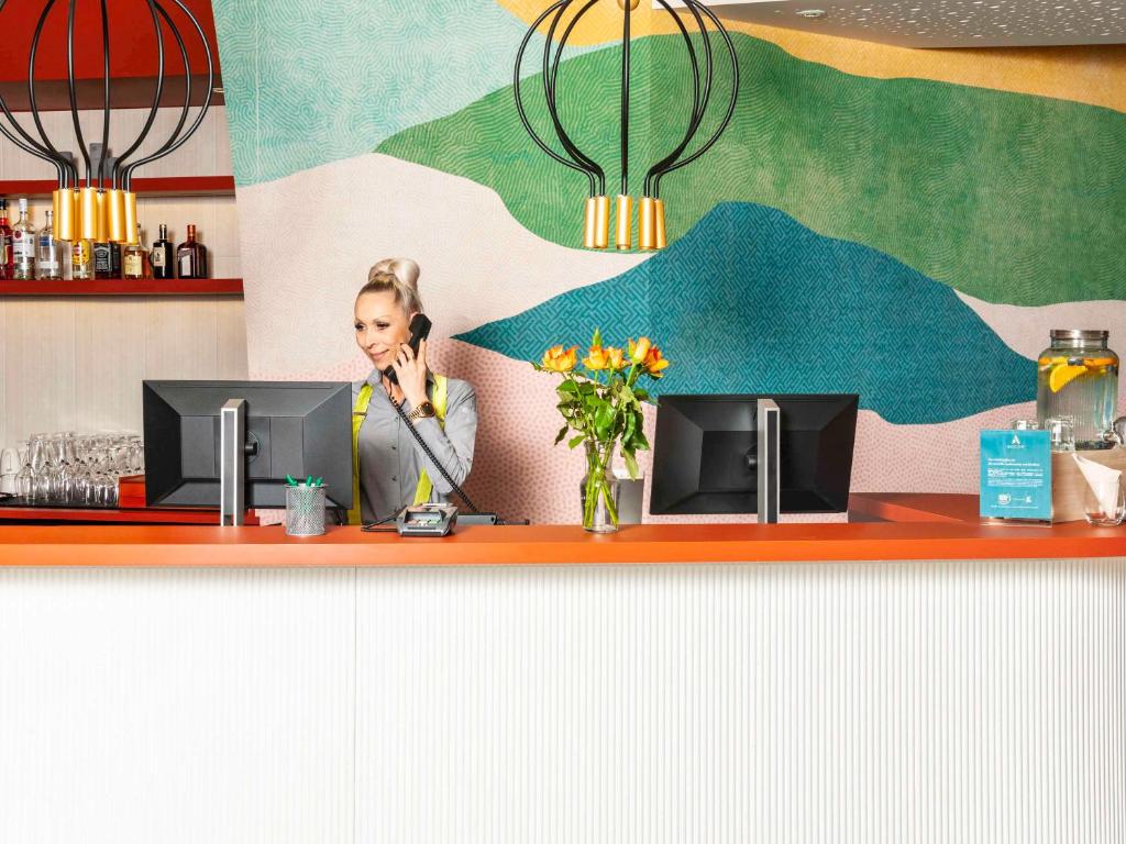 a woman sitting at a counter talking on a phone at ibis Styles St Margrethen Bodensee in Sankt Margrethen