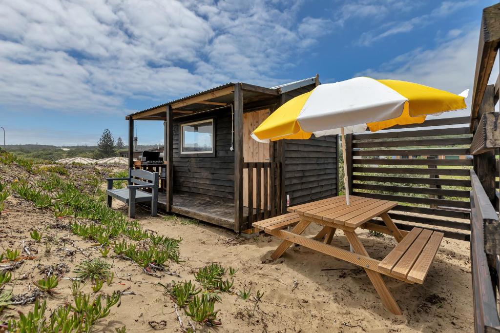 a picnic table and an umbrella on the beach at Karo Hut B - Ninety Mile Beachfront Cabin in Awanui