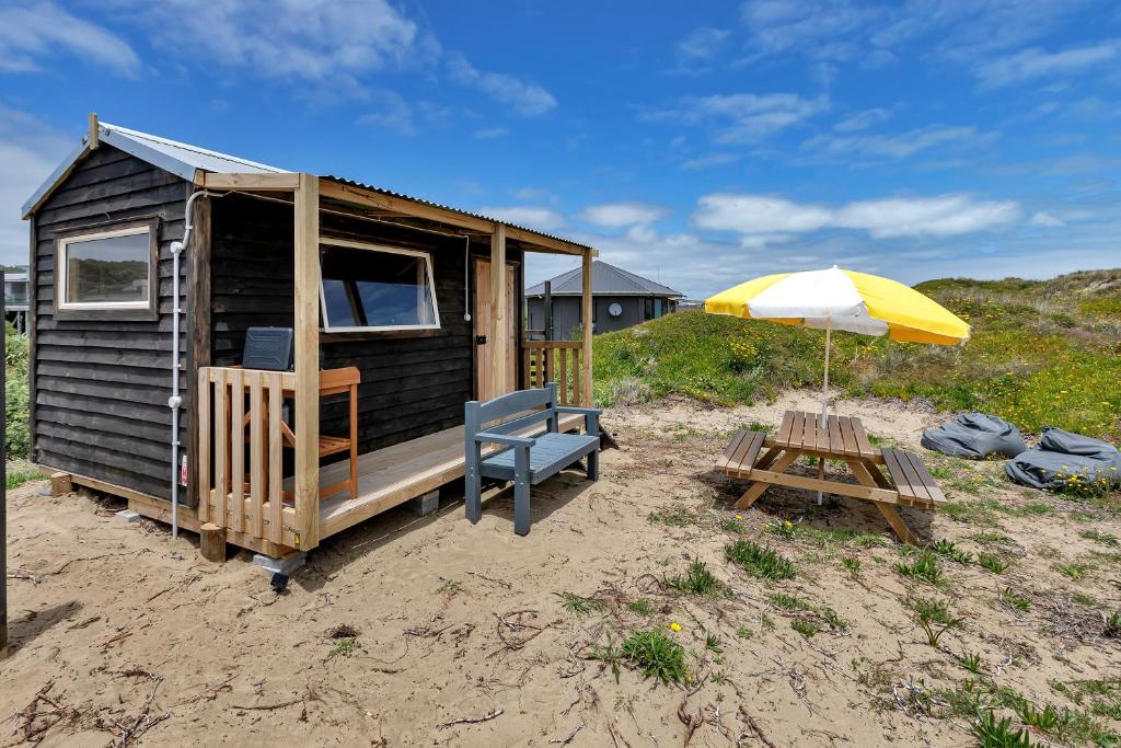 Cabaña pequeña con sombrilla y mesa de picnic en Karo Hut A - Ninety Mile Beachfront Cabin en Awanui