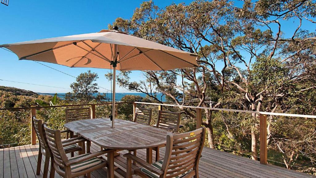 a wooden table with an umbrella on a deck at 'Charming Cottage Retreat' by HolidayCo in Killcare
