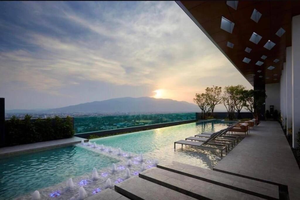 a swimming pool with chairs and a sunset in the background at Escent condo Chiangmai F17 in Chiang Mai