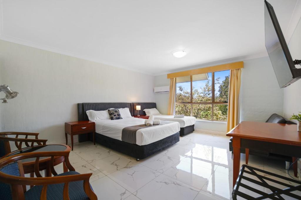 a bedroom with two beds and a desk and a window at Golf Place Inn Wollongong in Wollongong
