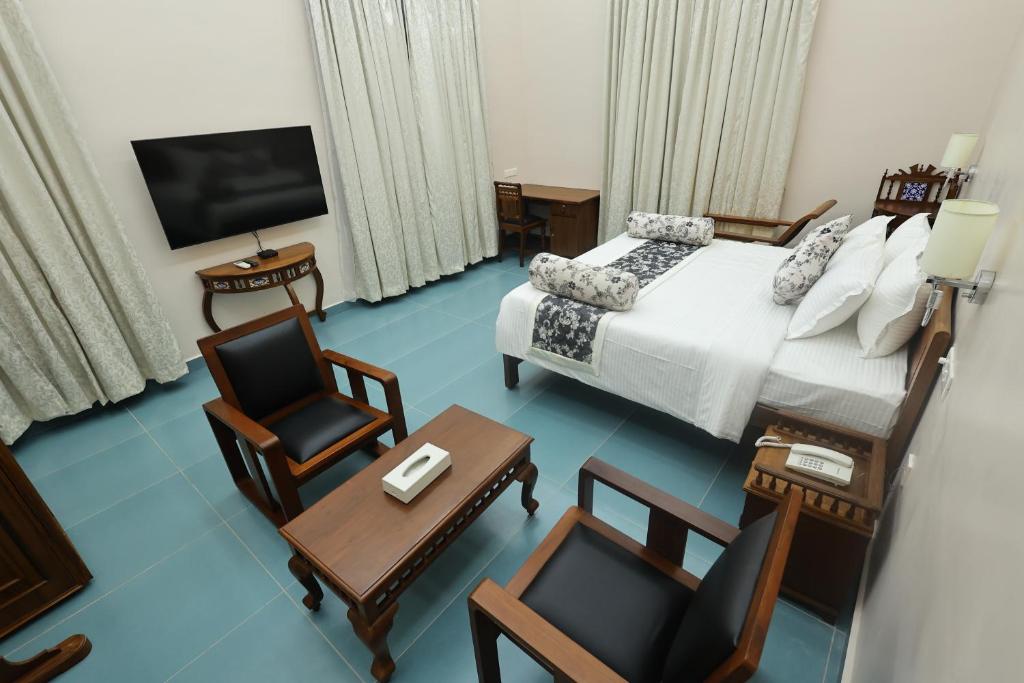 a hotel room with a bed and chairs and a television at Le Colonial Suites in Puducherry