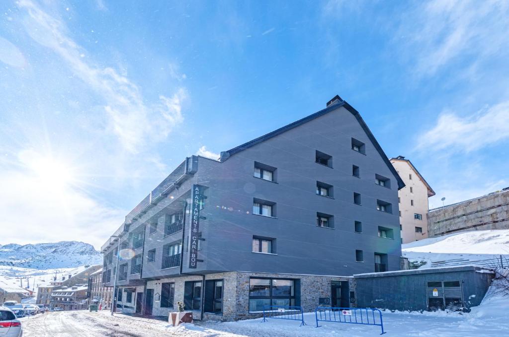 Un bâtiment dans la neige avec le soleil derrière lui dans l'établissement Apartamentos Caribou, au Pas de la Case