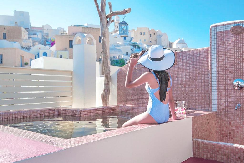 a woman in a blue dress and hat sitting on a ledge at Luxury Villas Hariton in Emporio Santorini