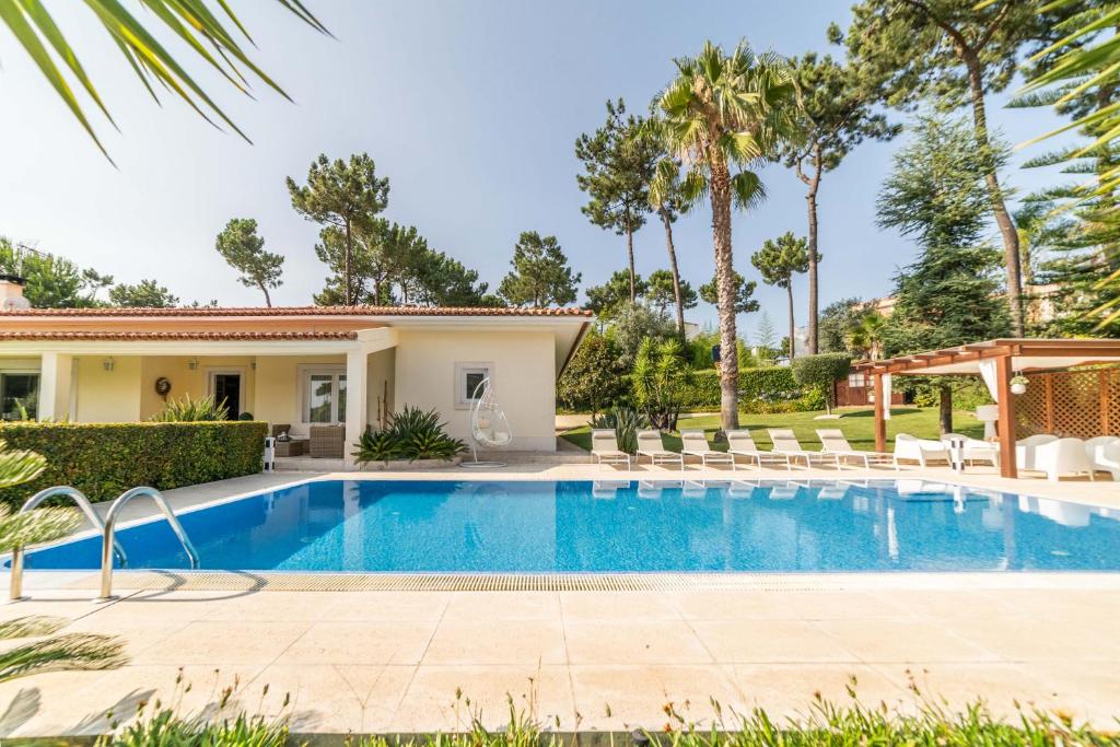 uma piscina em frente a uma casa com palmeiras em Villa Alecrim em Aroeira
