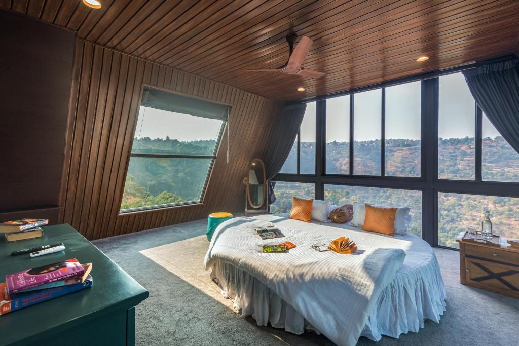 a bedroom with a bed with a desk and large windows at SaffronStays A Vantage, Panchgani - A Pyramid Shaped Unique Luxury Villa With Infinity Valley Views in Panchgani