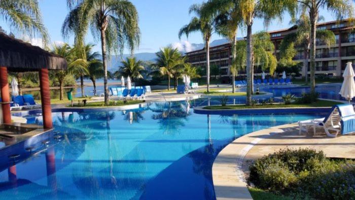 uma grande piscina com palmeiras e um hotel em Flat em Resort Paradisíaco! em Angra dos Reis