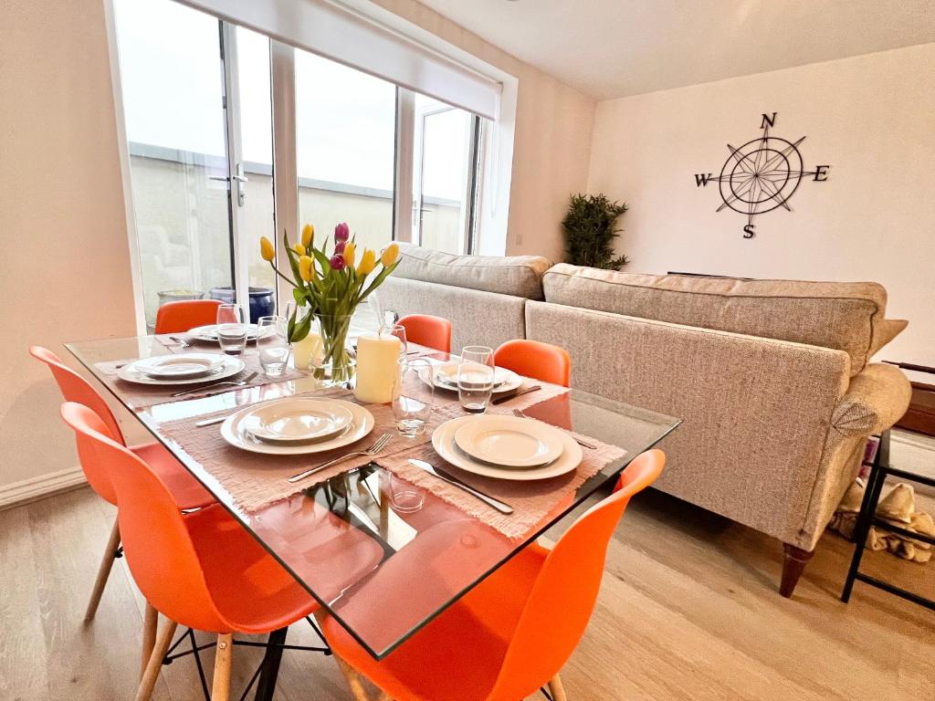 ボアハムウッドにあるSpacious 3-bed top-floor flat w/ balconyのダイニングルーム(ガラステーブル、オレンジの椅子付)
