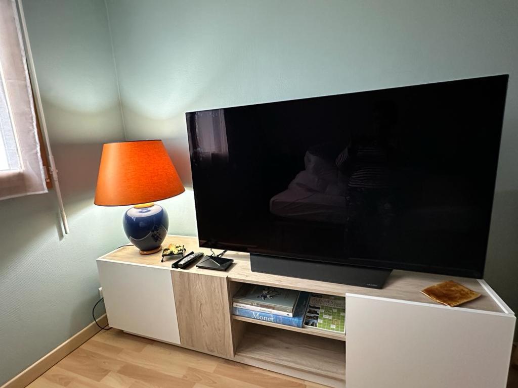 a large flat screen tv on a stand with a lamp at Chambre Céladon in Changé
