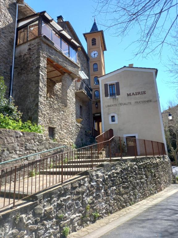 a building with a clock tower next to a stone wall at L&#39;Armandière, maison de caractère où règne calme et sérénité. in Pézenes-les-Mines