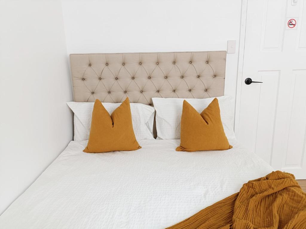 uma cama branca com almofadas laranja em Stunning Queen Room 1Min Walk to Station with 55 Inch TV em Sydney