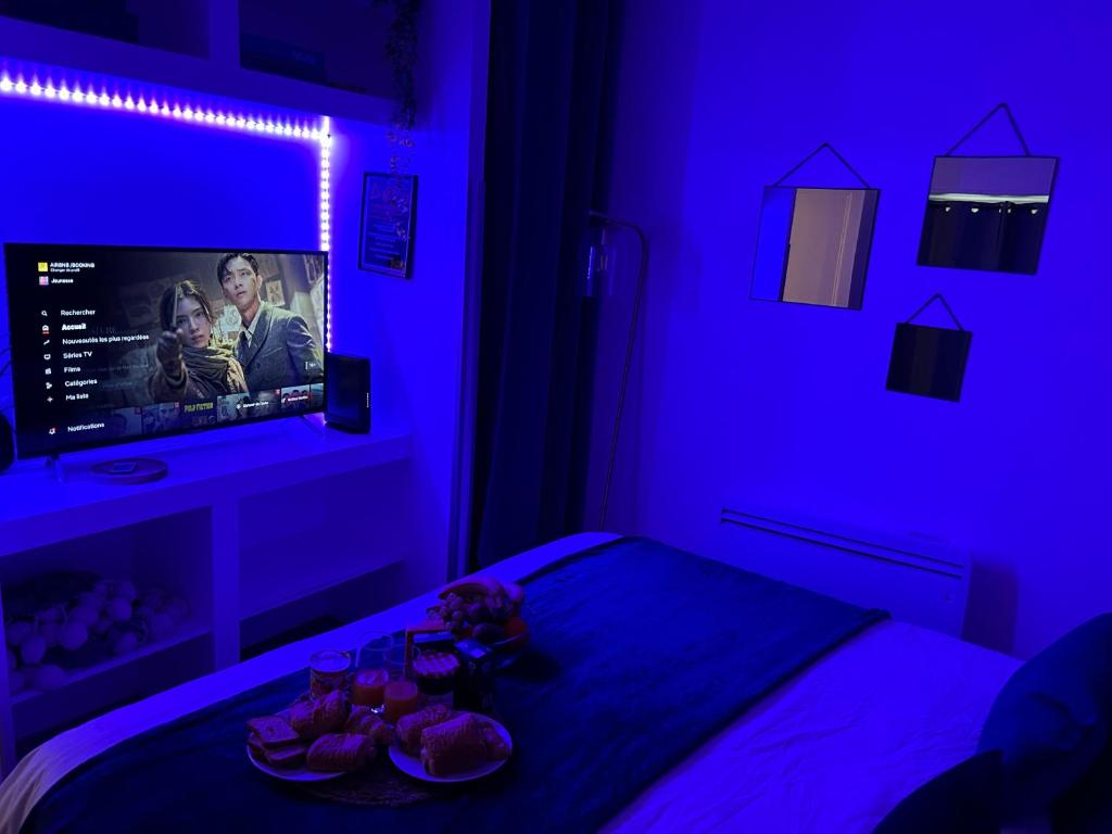 1 dormitorio con luces moradas y 1 cama con TV en Appart' Studio cooconing - Champs Elysées - JO 2024, en Maisons-Laffitte