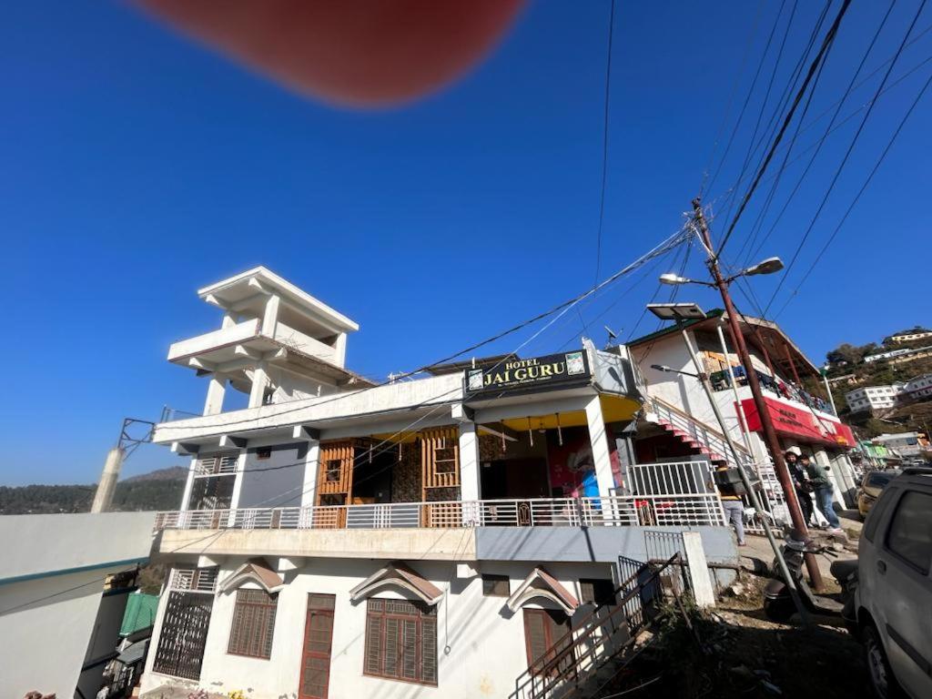 a white building with a balcony on a street at Hotel Jai Guru in Almora