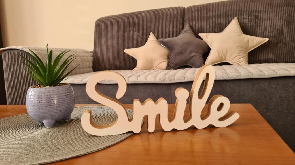 a wooden sign that says smile on a table in front of a couch at Apartman Enjoy Arandjelovac in Arandjelovac