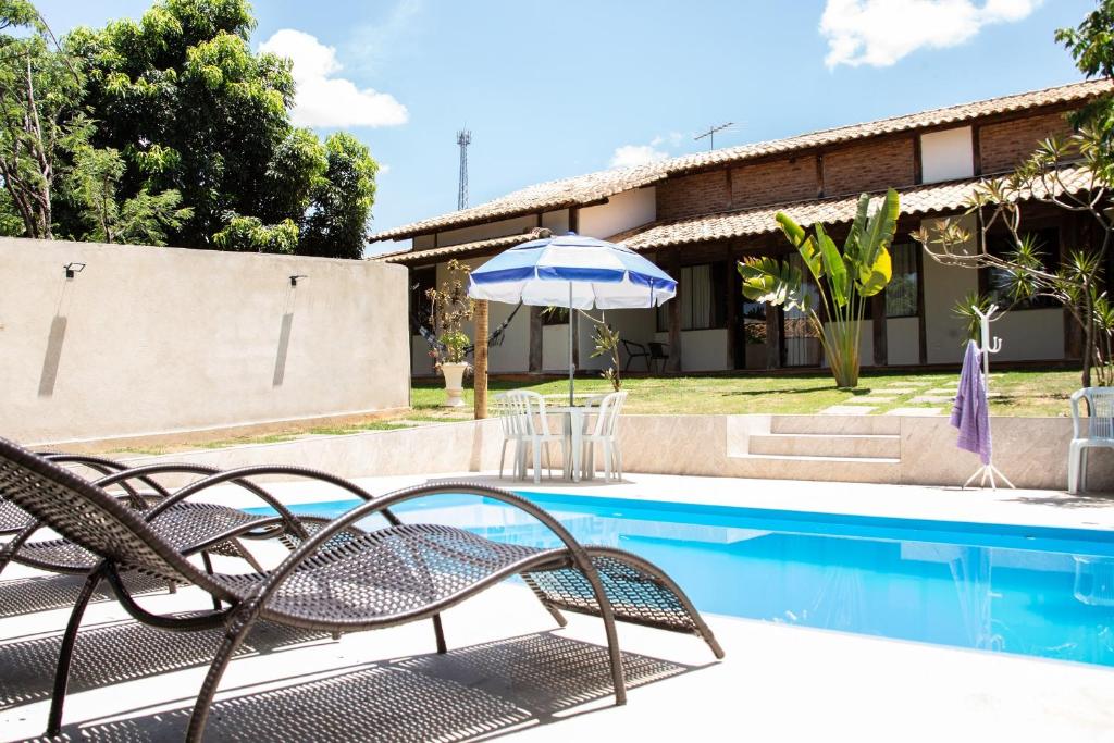 a pool with chairs and an umbrella next to a house at Casa das Pedras in Lagoa Santa