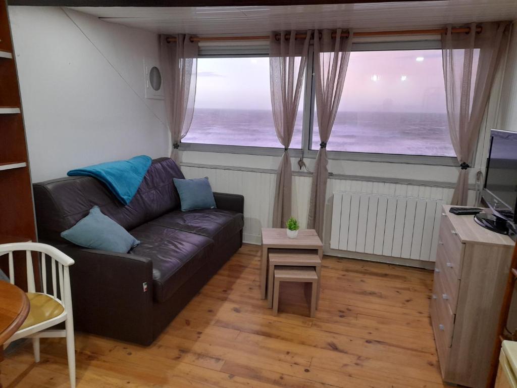 een woonkamer met een bank en 2 grote ramen bij L'Anéda - STUDIO vue panoramique sur Mer - 2 personnes - Animaux OK - Wifi in Mers-les-Bains