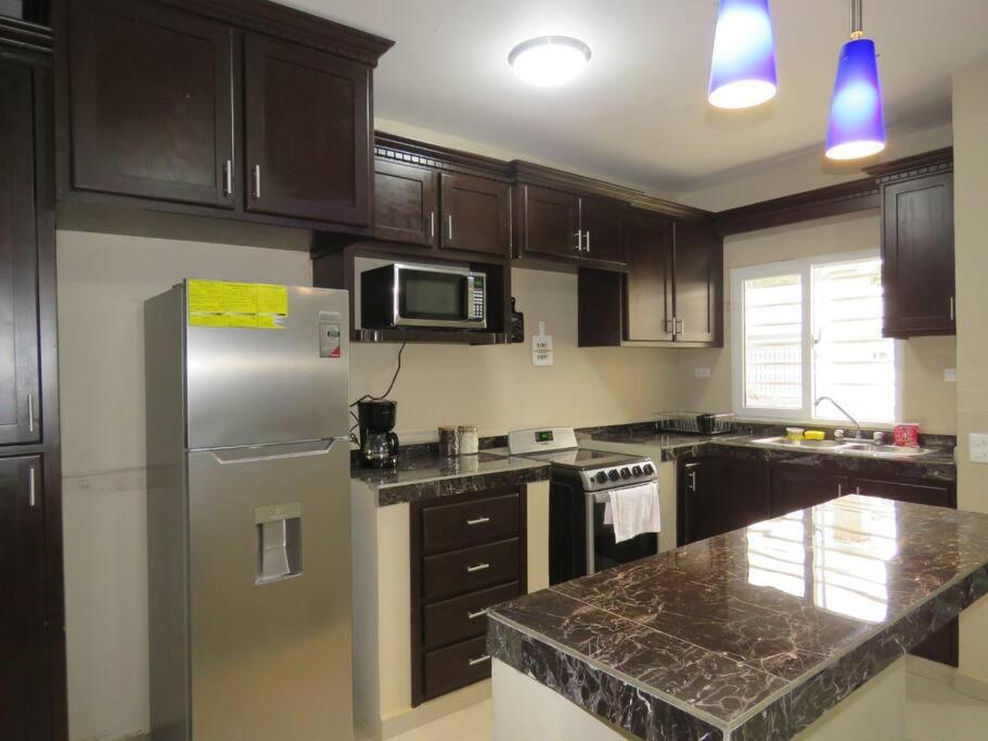 a kitchen with wooden cabinets and a stainless steel refrigerator at Casa en Ceiba 15 min de la playa in La Ceiba