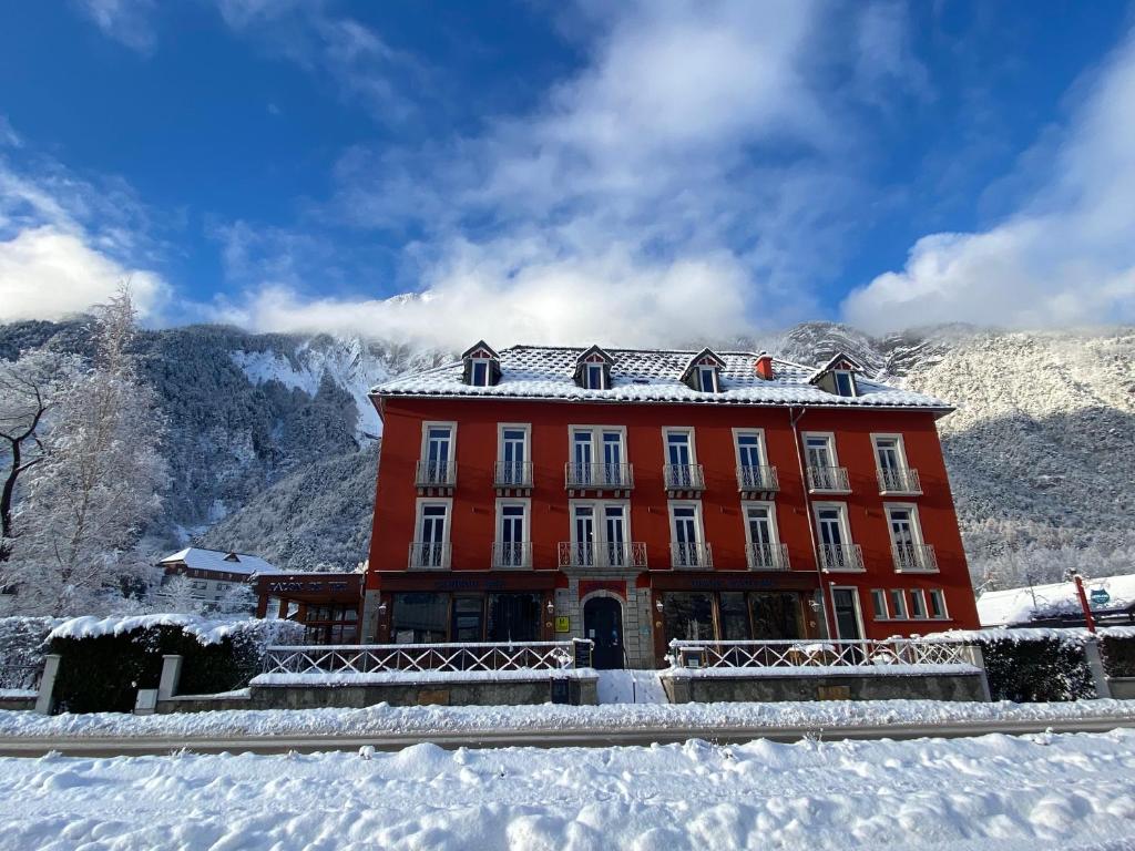 a red building in the snow with mountains in the background at hôtel oberland in Le Bourg-dʼOisans