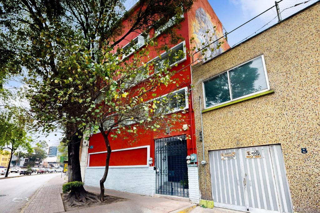 ein rotes Gebäude mit einem Baum davor in der Unterkunft Cadetes 47 #302 in Mexiko-Stadt