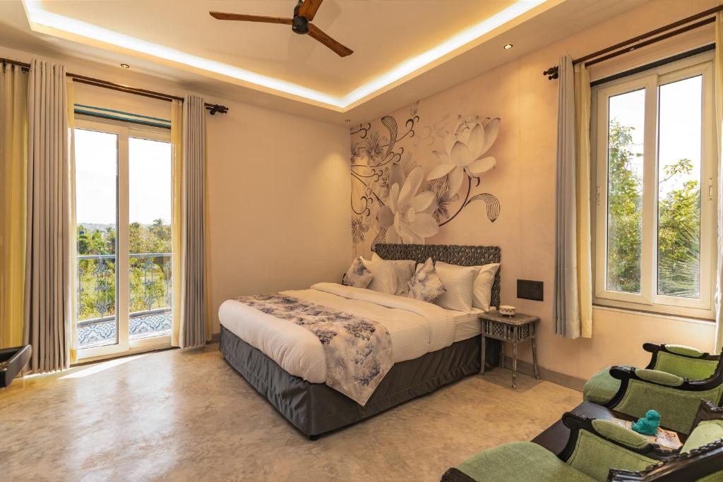 1 dormitorio con 1 cama, 2 sillas y ventanas en Lotus Villa Goa en Mandrem
