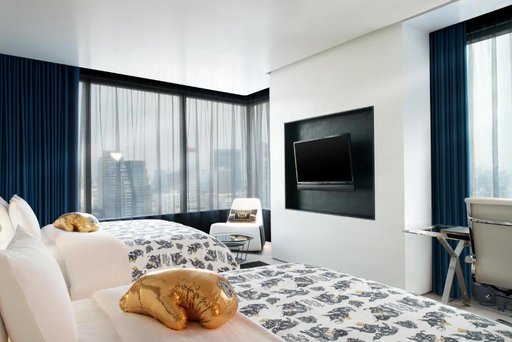 A twin room arranged around a wall-mounted television and corner windows over the city.