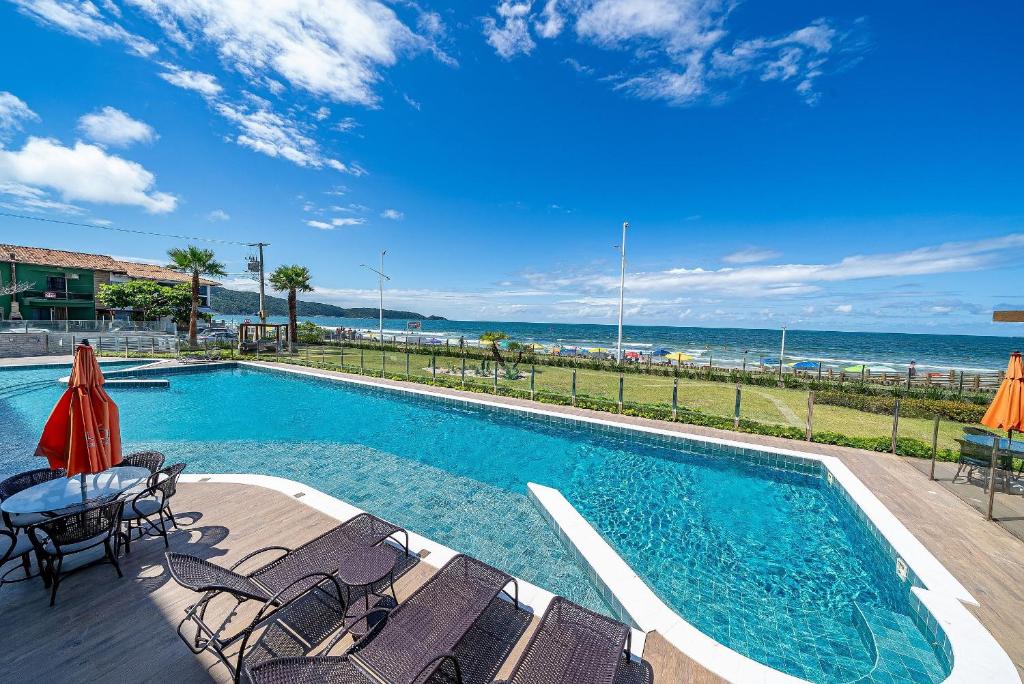 a swimming pool with chairs and the ocean in the background at Edifício Solar do Atlântico Beira Mar de Bombas in Bombinhas