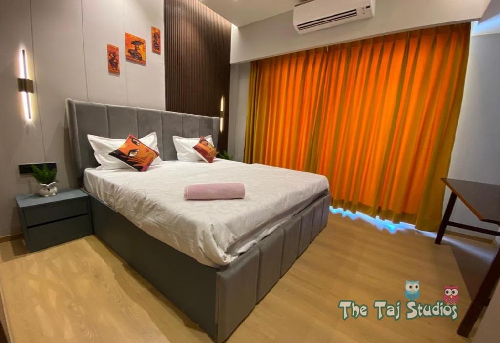 1 dormitorio con 1 cama con cortina naranja en Taj Studios - Luxury Suit at Blue Sapphire Mall #US Cinema #PizzaHut #HIRA Sweets #Food Court etc by GHUMLOO-COM, en Ghaziabad