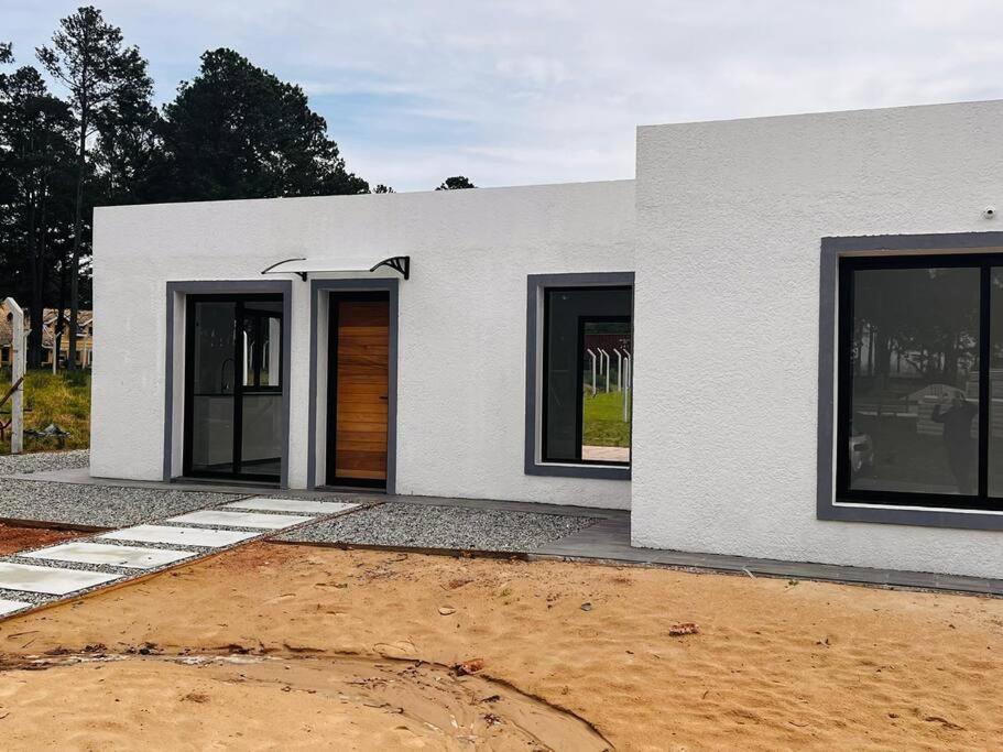 una casa blanca con un patio de tierra delante de ella en CASA moderna en la floresta a 5 minutos de Punta Ballena, en Maldonado