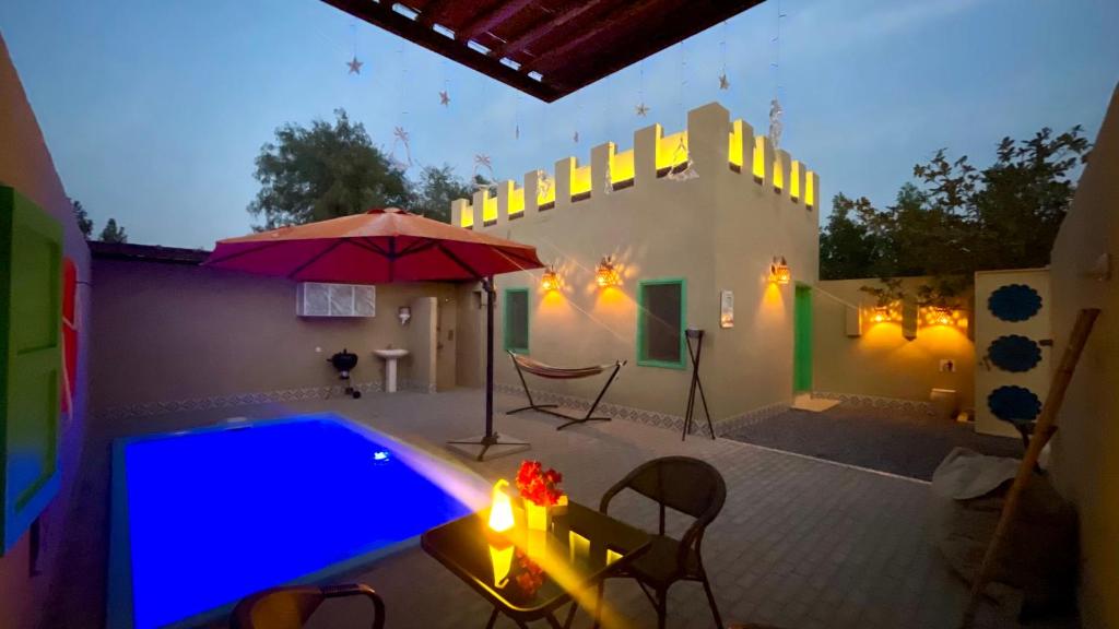 a patio with a pool and an umbrella and a table at Al Bait resort with private swimming pools -HRS stables in Al Ḩamrānīyah