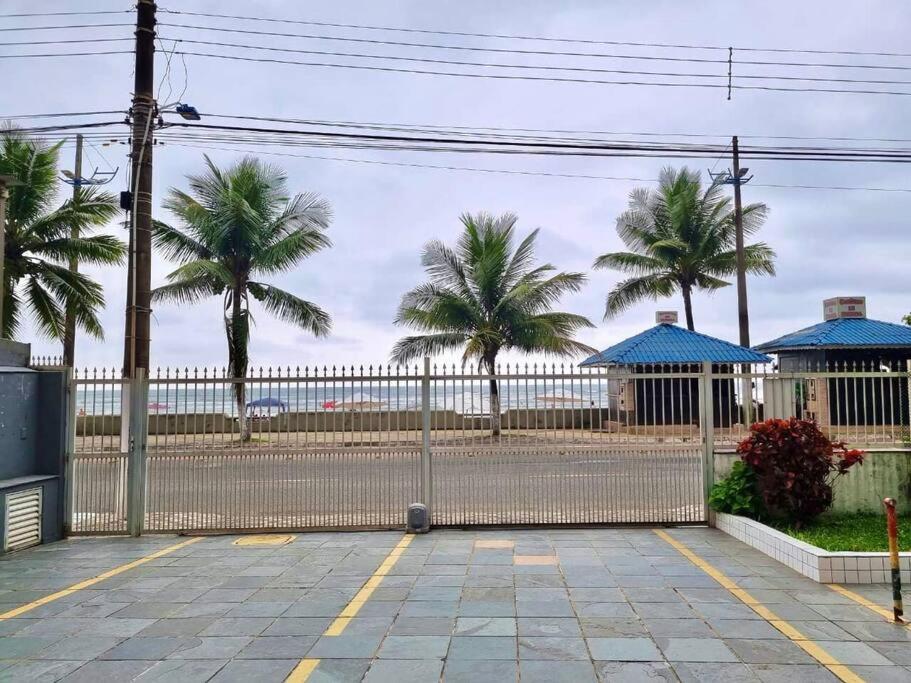 a fence with palm trees in front of a beach at Apartamento para alugar in Mongaguá