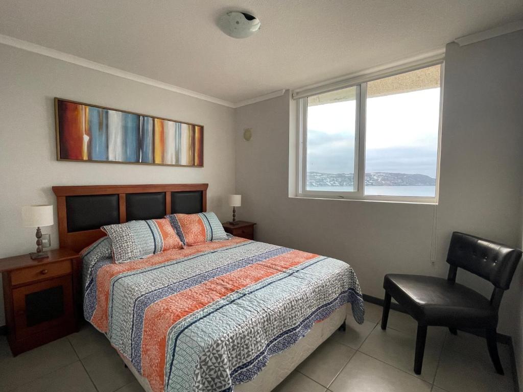 a bedroom with a bed and a chair and a window at Apartamento junto a la playa en Bahía Horizonte in Coquimbo
