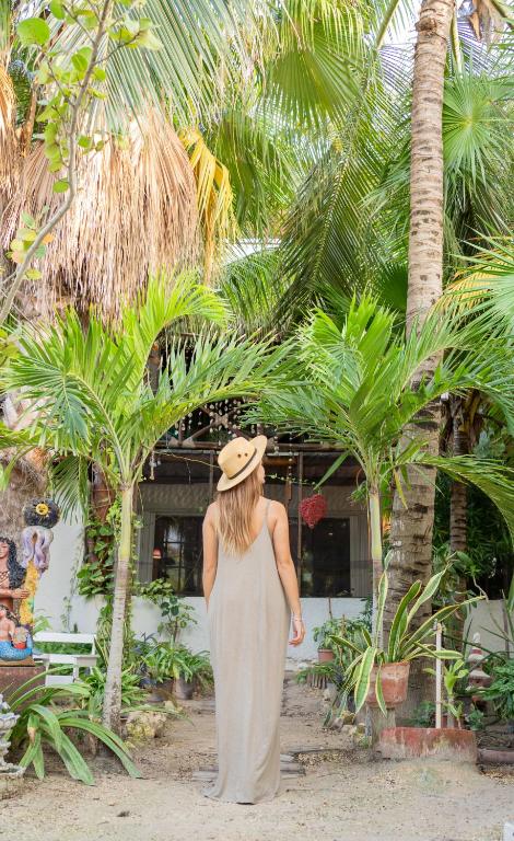 a woman wearing a hat standing in front of palm trees at Sirenas Caribbean Rooms Holbox in Holbox Island