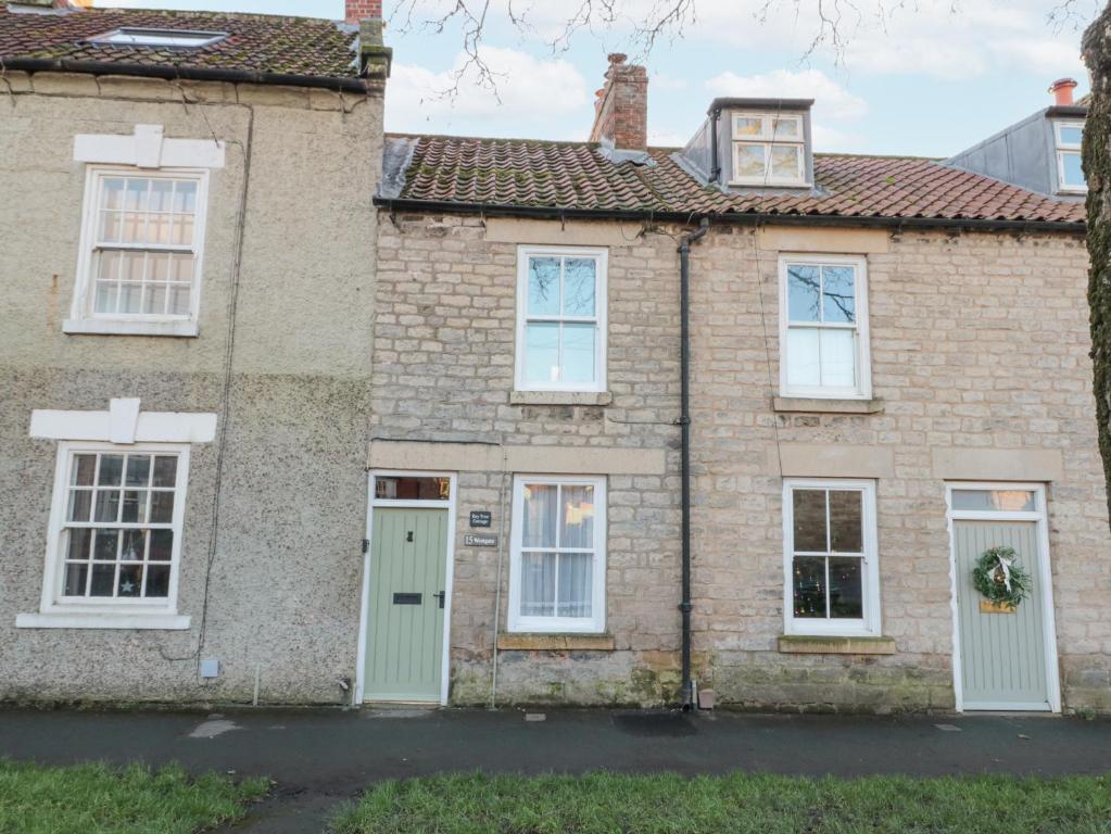 an old brick house with white windows and a green door at Bay Tree Cottage in Pickering