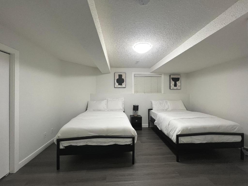 duas camas num quarto com lençóis brancos em Cozy Suite Near Airport Calgary em Calgary