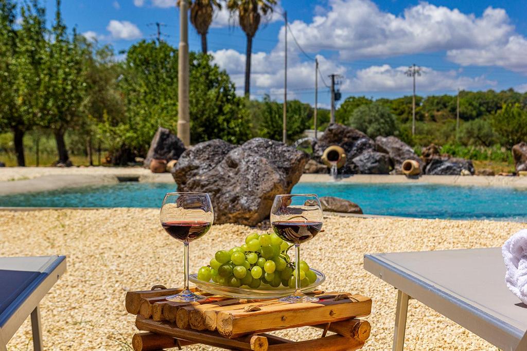 dos copas de vino en una mesa junto a una piscina en Casale Buona TerraMia, en Castiglione di Sicilia