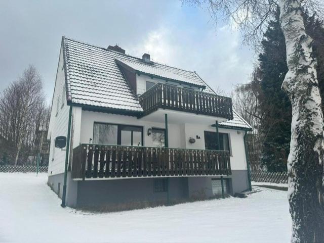 une maison blanche avec une terrasse dans la neige dans l'établissement Haus Leni am Paulsberg, à Braunlage