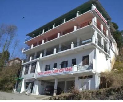 a large white building with a sign on it at Hotel Manali Jain Cottage in Manāli