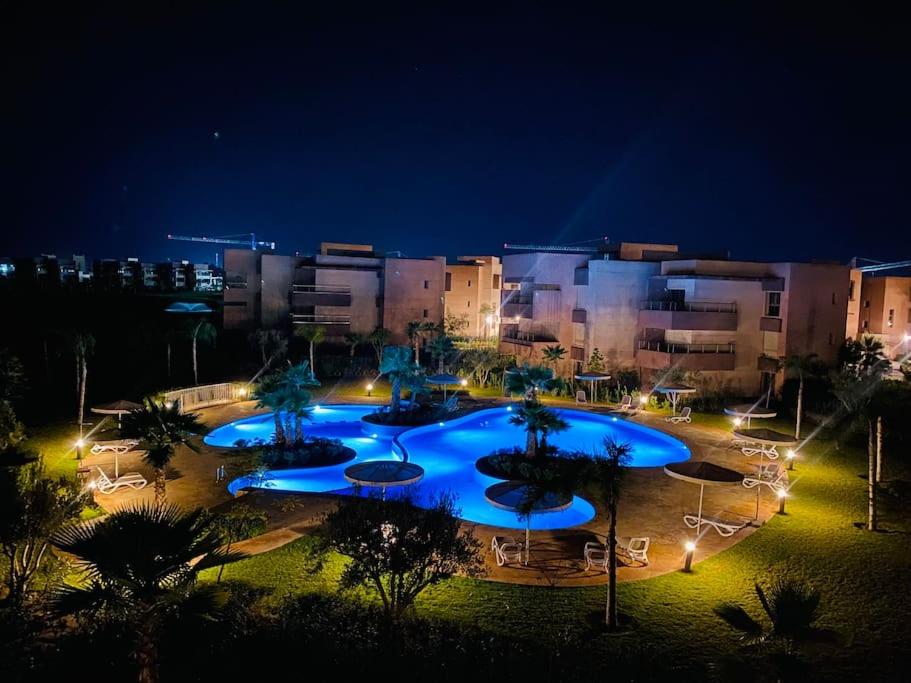 Luxueux Appartement Prestigia في مراكش: مسبح كبير مع أضواء زرقاء أمام المبنى