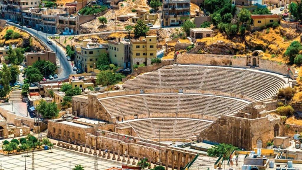 an ancient amphitheater in a city with buildings at Conord Hotel - "Amman's Heart" in Amman