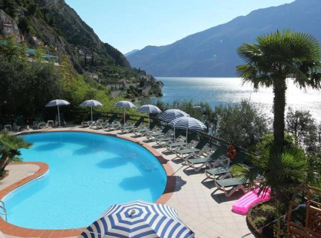 a swimming pool with chairs and umbrellas and the ocean at Hotel Augusta Garnì in Limone sul Garda