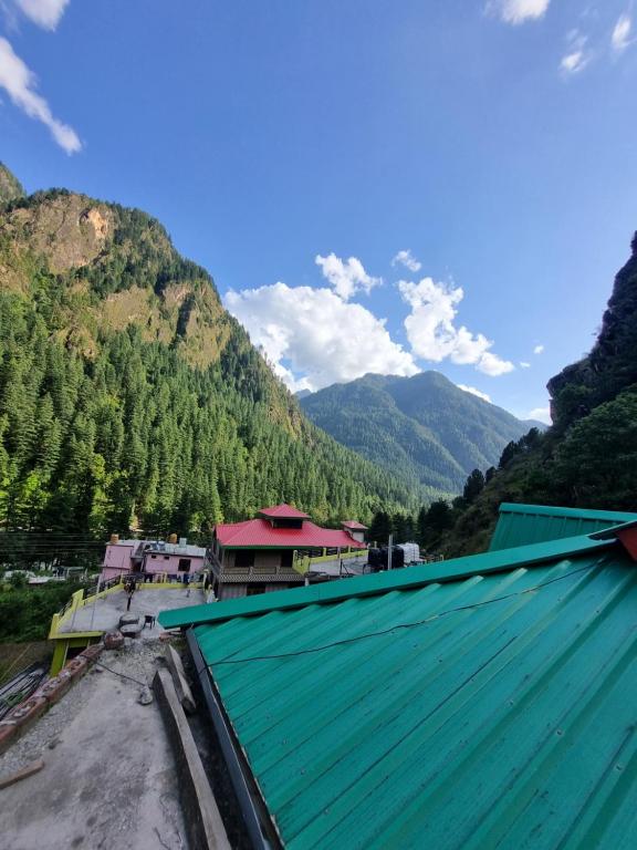 a building with a green roof with mountains in the background at Shanti guest house chojh in Kasol