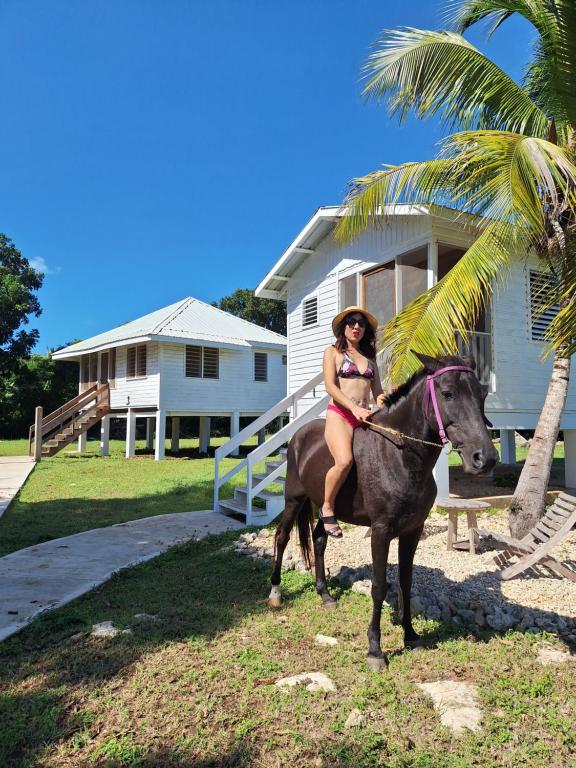 a woman in a bikini riding a horse in front of a house at Horse Cottage in Sarteneja